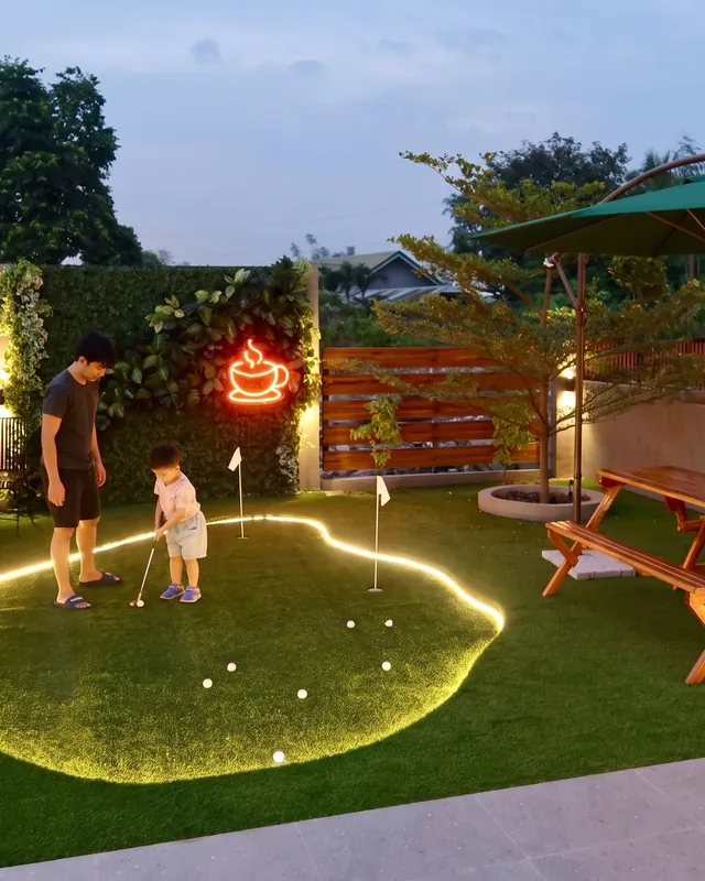 A parent and child on the lit putting green in Manna's garden